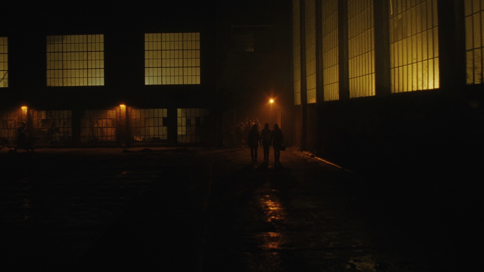 Moody night exterior of an urban warehouse building glowing with warm amber light